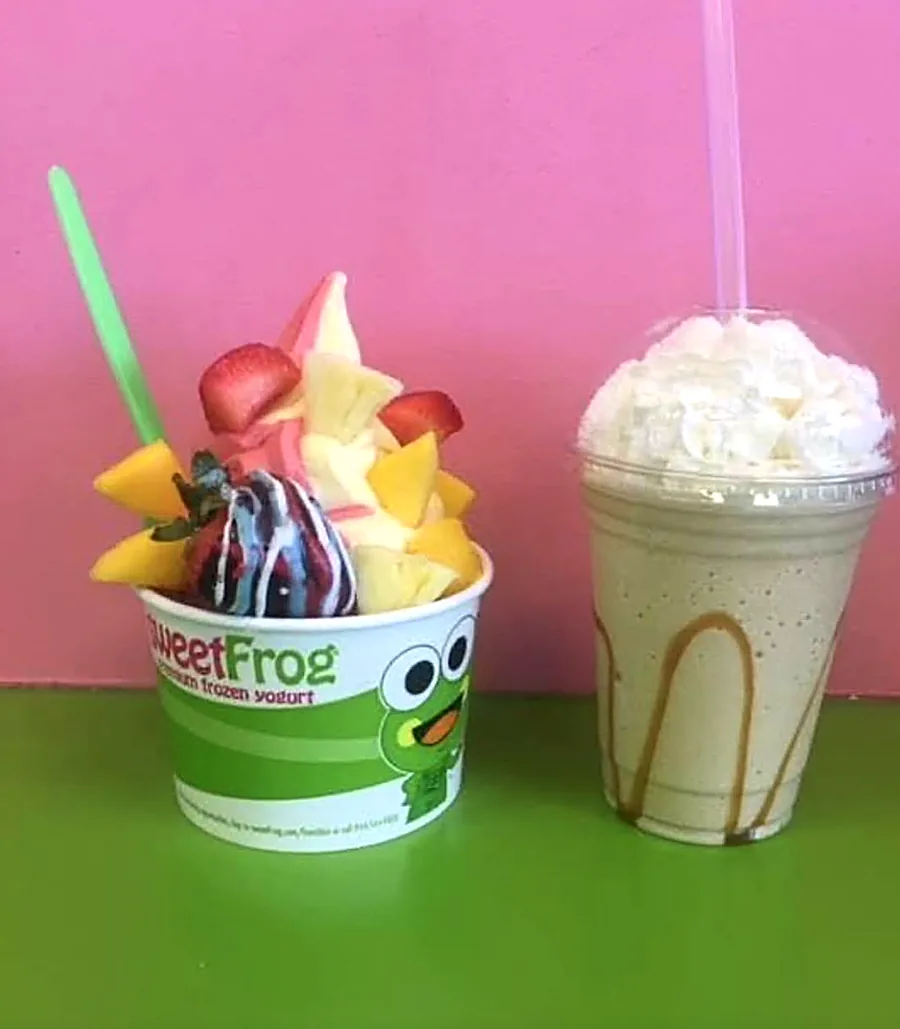 A sweetFrog frozen yogurt cup with fresh fruit next to a caramel shake
